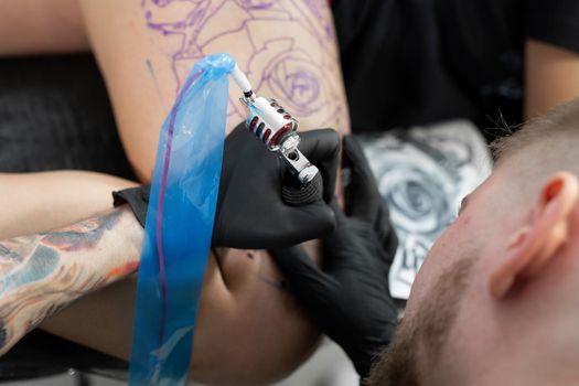 Close up image of the bearded tattoo male artist makes a tattoo on a female leg