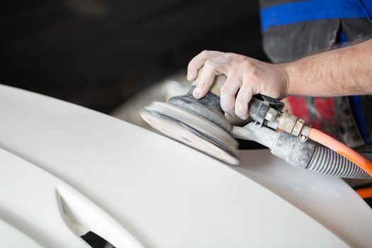 A man who sanding with a grinder and prepares the paint for the car in a car service. Repairman fix car paint.