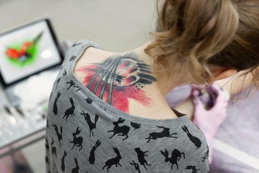 Close-up of a female artist making a color tattoo on the leg of a young girl. Rear view from the back