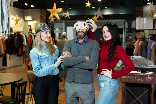 Portrait of beautiful two women and a man in a sleeping mask in a clothing store