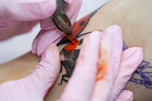 Needle tattoo machines inject a red ink into the skin of a girl. Close-up of the process of applying the tattoo on the skin