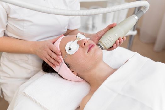 Professional cosmetologist is making cavitation rejuvenation skin treatment. Young woman is lying and relaxing. Radio wave lifting