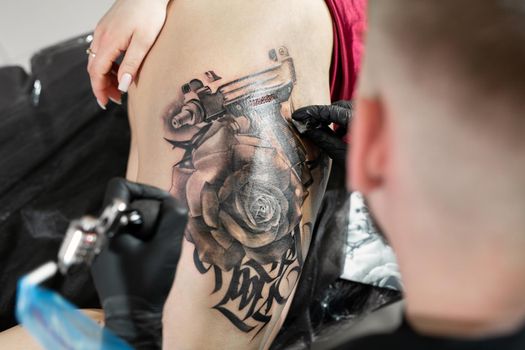 Close up image of the bearded tattoo male artist makes a tattoo on a female leg