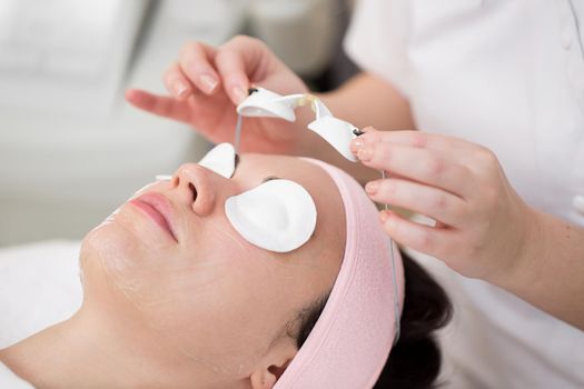 Close-up of a beautician take off protective glasses from a girl's eyes after a cosmetic procedure. Process of radio wave lifting in the spa salon