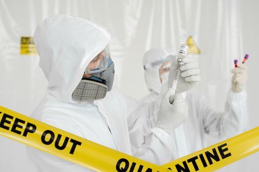 Doctor in a protective suit and mask holds an injection syringe and vaccine COVID-19. Laboratory Scientists in a Coverall Conducting a Research Vaccine.