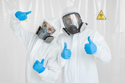 Portraits of the doctor: a man and a woman in protective suits and respirators, wearing gloves, show the thumbs up during quarantine. Covid-19.