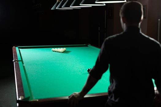 A man plays Billiards. The view from the back
