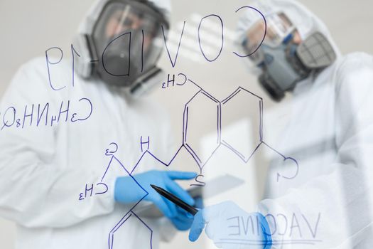 Scientists in chemical protective suits are writing formula on glass board at laboratory. Concept of Covid-19.
