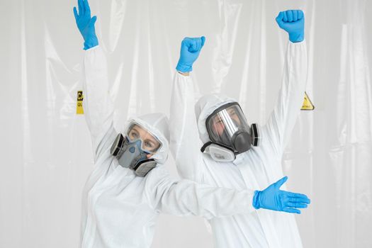 Portraits of a doctor: a man and a woman in protective suits and respirators, wearing gloves, having fun during quarantine. Covid-19.