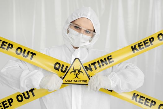 Epidemiologist woman in protective clothing is in a restricted area with a danger sign. Yellow line Keep Out Quarantine. Quarantine alert sign. Entrance is forbidden in quarantine zone