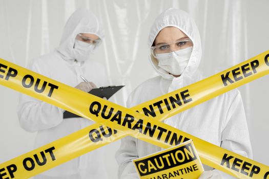Epidemiologists a man and a woman in protective clothing are in a restricted area with a danger sign. Yellow line Keep Out Quarantine. Quarantine alert sign. Entrance is forbidden in quarantine zone