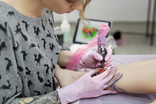 Professional tattoo artist which making tattoo on the leg of a young girl. Hands of a tattoo artist. Tattooist makes a tattoo