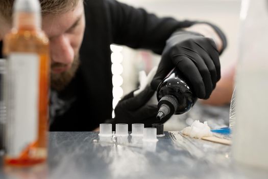 Tattoo master pours black paint. Tattoo artist prepares tools and ink before working in a tattoo parlor.