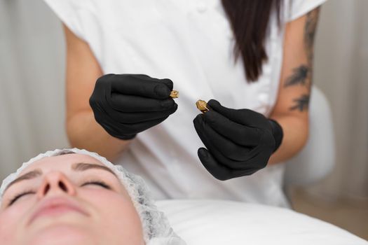 Close-up of a beautician doctor in black sterile gloves opens an ampoule with hyaluronic acid before the rejuvenation procedure