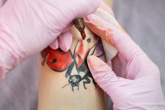 Needle tattoo machines inject a red ink into the skin of a girl. Close-up of the process of applying the tattoo on the skin