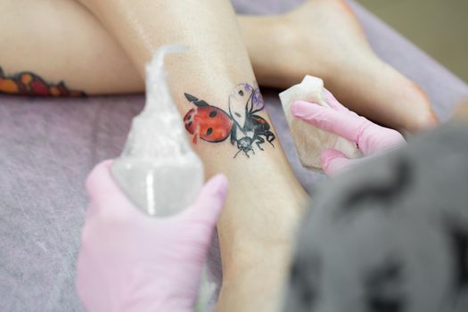 Close-up of a female artist making a color tattoo on the leg of a young girl. Tattoo artist stuffs a ladybug on a girl's leg, tattoo for a girl