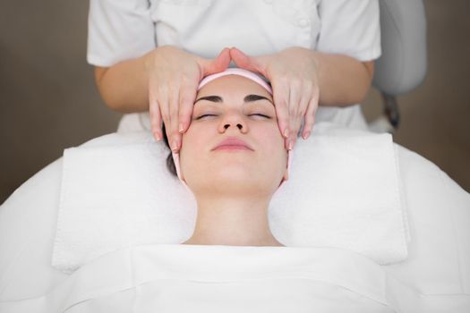 Beautician makes a professional massage of the face of the neck and shoulders for a young girl in the Spa salon. The view from the top. Facial beauty treatment