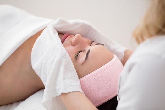 Hands of the beautician wipe the girl's face in the cosmetology center with white gloves. Portrait of a beautiful girl on the procedure for rejuvenating the face in a beauty salon