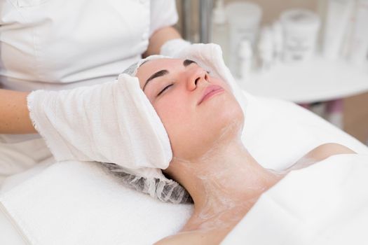 Hands of the beautician wipe the girl's face in the cosmetology center with white gloves. Portrait of a beautiful girl on the procedure for rejuvenating the face in a beauty salon