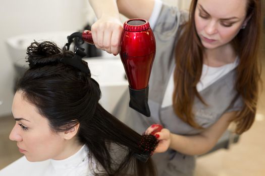 Portrait of a woman hairdresser who works with a client in a beauty salon. Hairdresser dries wet hair girl with a hair dryer
