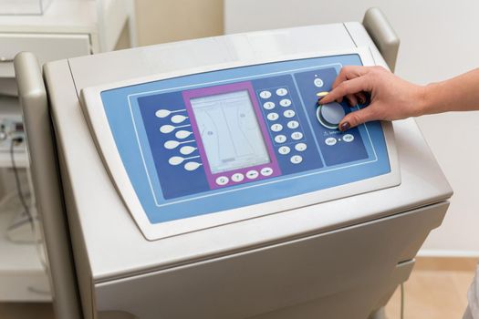 Cosmetologist works with cosmetology medical equipment, twists the lever and presses buttons on the screen. Beautician works on the biostimulation apparatus making the girl a massage