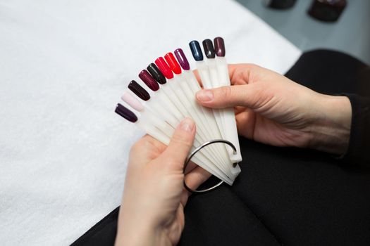 Manicure and nail care concept. A woman in a beauty salon holds colored test nail polishes with different colors and chooses the color for painting.