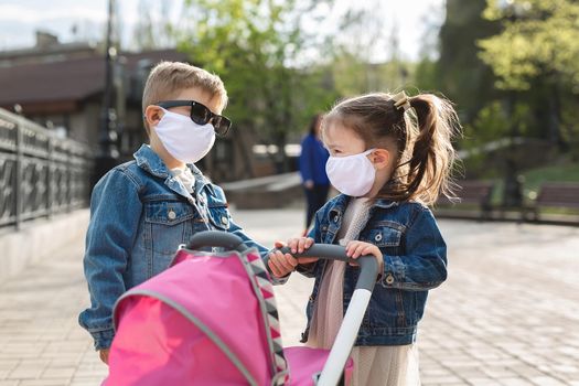 Boy and a girl walk with a pram in protective face masks. Concept of family. Coronavirus, covid-19