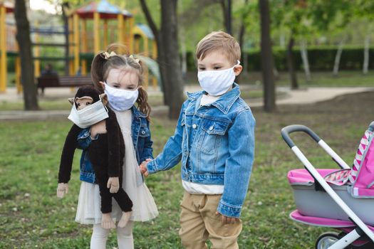 Child boy and girl walking outdoors with face mask protection. Little girl holds a stuffed monkey in her hands. Coronavirus, covid-19