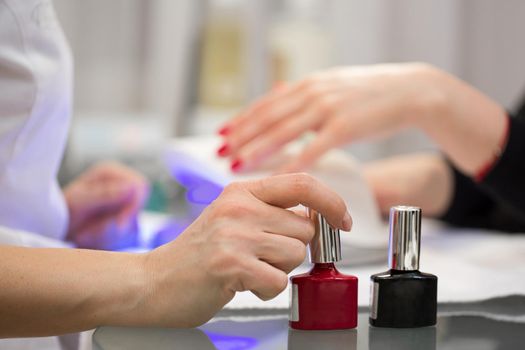 Manicurist master makes red manicure on young woman hand. Woman nail master doing nails to a girl client at a beauty salon. Care for hands