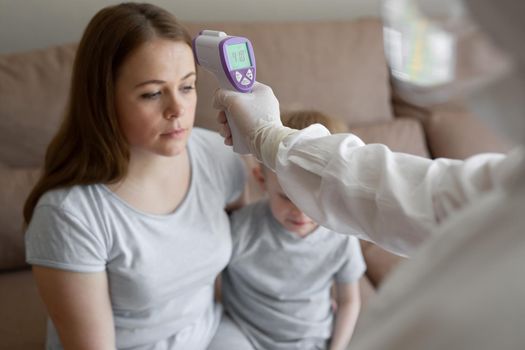 Doctor check patient body temperature using infrared forehead thermometer gun at home. Coronavirus, covid-19, high fever and cough.