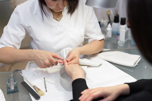 Nail Salon. Closeup Of Female Hand With Healthy Natural Nails Getting Nail Care Procedure. Hands Removing Cuticles With Professional Nail Tool, Metal Clippers. Beauty Manicure