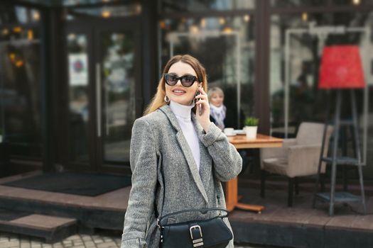 Beautiful young woman in sunglasses is talking on the phone while her elderly mother is waiting in a cafe on the street.