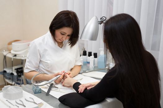 Manicurist doing hardware manicure to a young beautiful girl in the spa salon. Hardware manicure. Concept of body care