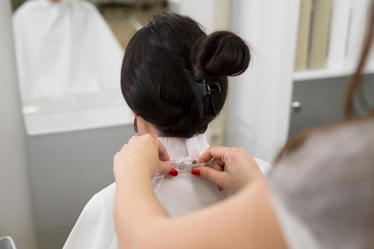 Close-up of a hairdresser fixing a collar and a cape on the neck of a young girl in a hairdressing salon