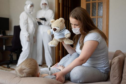 Mom measures baby's temperature. Doctors in protective suits at sick patients at home. Coronavirus, covid-19.