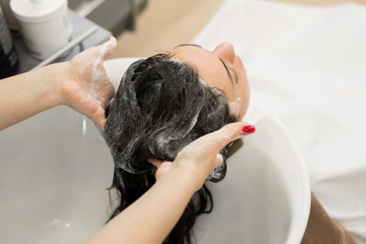 Young girl hairdresser washes her hair with shampoo and massages the head of a young woman in a modern barber salon