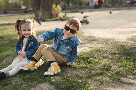 A little happy cute boy and a little cute girl sitting on the grass in a beautiful place