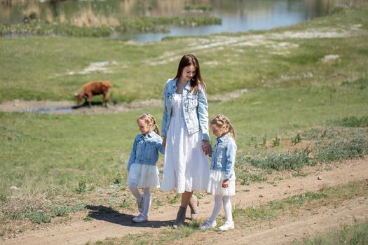 Young mother and her twin daughters are walking along a path in the village.