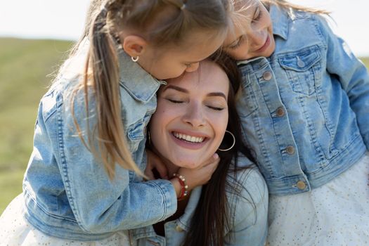 Close-up portrait of a mother and twin daughters hugging and smiling in nature.