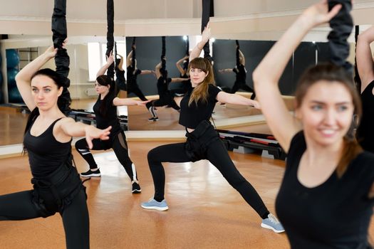 Group of active sports girls in black sportswear are engaged in budgie fitness in the gym. Bungee jumping in the gym