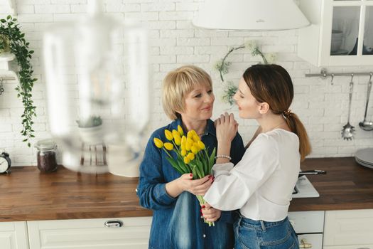 Beautiful adult woman is giving flowers to her mature mother. Women's day