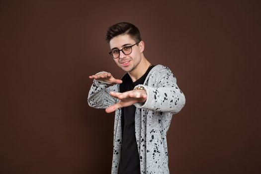 Close up portrait of an excited happy man in eyeglasses pointing fingers at camera isolated on the brown background