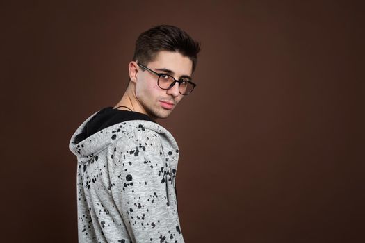 Young man in depression. Stylish male student wears round spectacles, has trendy hairstyle, looks confidently, isolated over brown background. People and human expressions