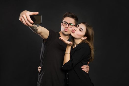 Happy young loving couple making selfie and smiling while standing against black background