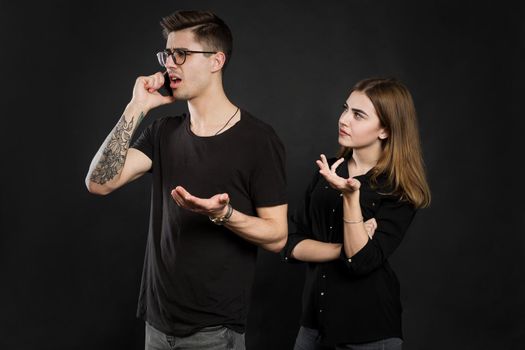 Portrait of a young couple standing with mobile phone, man is using mobile phone while angry girl standing near isolated over black background