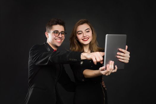 Happy couple pointing finger at digital tablet isolated on black background