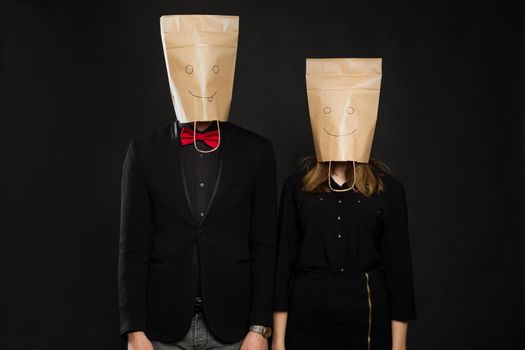 Young couple with bags over heads on black background
