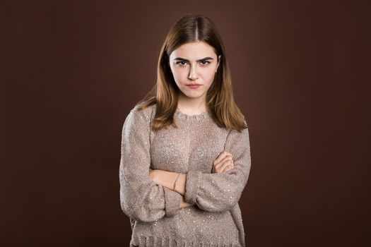 Portrait of beautiful girl frowning her face in displeasure, wearing loose long-sleeved sweater, keeping arms folded. Attractive young woman in closed posture.