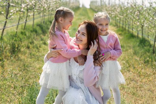 Portrait of a mother and her twin daughters in a blooming Apple orchard.