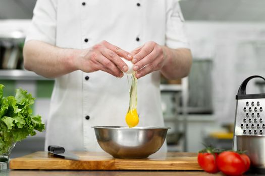 Cook breaks an egg. Egg yolk falling into the bowl